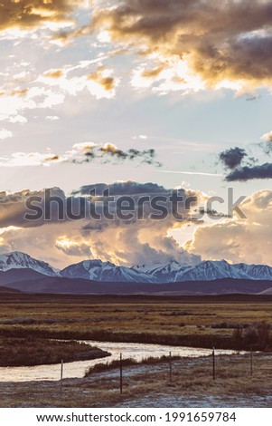 Owens River runs though Arid plains against Sierra Nevada Mountains and dramatic sunset sky in the Owens River Valley near Mammoth Lakes