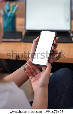 Close-up of businesswoman holding a smartphone blank white screen sitting at the office. Mock up.