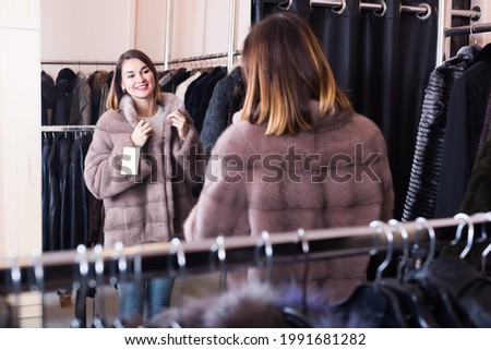 Young girl customer deciding on the choice of fur coat in women cloths store