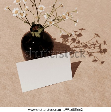 Card mockup with copy space and camomile flowers in a vase on beige background. top view. Greetings, wedding invitations blank, paper sheet.  