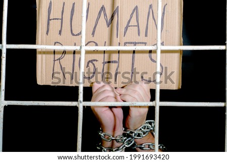 concept human rights freedom of speech hands shackled with an iron chain hold a cardboard sign with the inscription human rights behind an iron grate. High quality photo