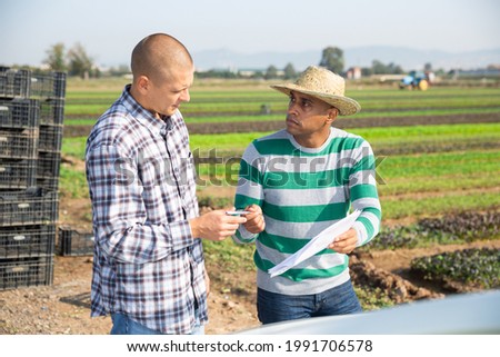 Farmer and worker signing some papers while standing near car on farm on sunny spring day