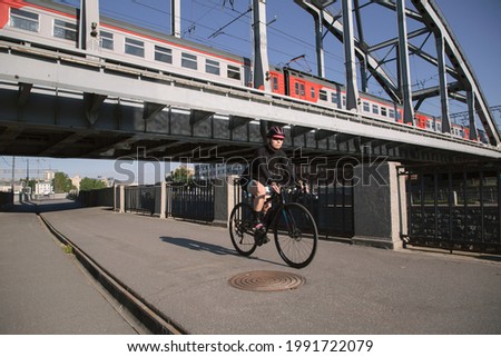 Morning training of female cyclist riding along the embankment under the railway bridge with a train at sunset. Sports in the city. Sports equipment.