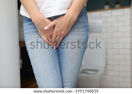 Woman stands in bathroom and covers her lower abdomen with her hand Royalty-Free Stock Photo #1991748839