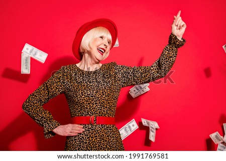Photo of aged woman happy positive smile look point finger empty space fly air cash dollars isolated over red color background