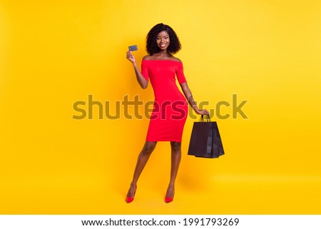 Full length photo of young afro girl happy smile hold credit card buy shop bags purchase sale isolated over yellow color background