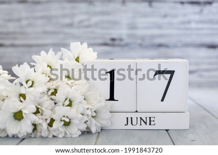 White wood calendar blocks with the date June 17th and white daisies. Selective focus with blurred background. 