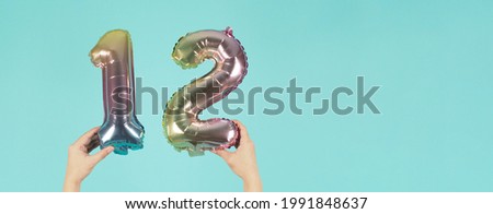 Hand is holding balloon number 1 2 or twelve on mint or tiffany blue background.