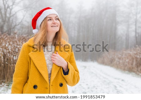 Happy young woman wearing a yellow coat, red hat smiling over nature background, trendy color of year 2021 - illuminatiing yellow and ultimate gray, winter time