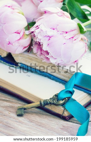 pile of vintage old books with peony flowers and key  stacked on table