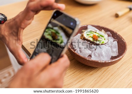 Anonymous man taking a picture with a phone of oysters with trout roe and coriander oil for social media and sharing with friends