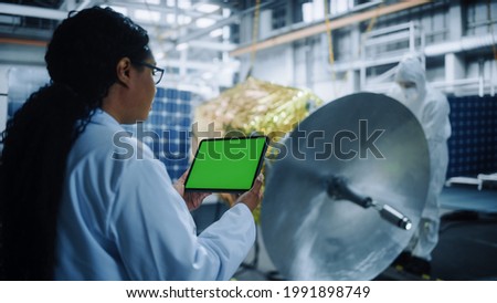 Female Engineer Uses Green Screen Tablet Computer while Working on Satellite Construction. Aerospace Agency: Scientists Assemble and Manufacture Spacecraft for Space Exploroation, Observation Mission