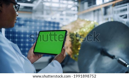 Female Engineer Uses Green Screen Digital Tablet Computer while Working on Satellite Construction. Aerospace Agency: Scientists Assemble Spacecraft for Space Exploration Mission. Over the Shoulder