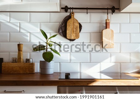 Kitchen brass utensils, chef accessories. Hanging kitchen with white tiles wall and wood tabletop.Green plant on kitchen background early morning light side view