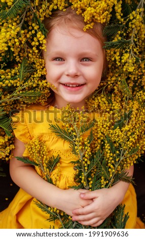 a child in a yellow dress lies in a field surrounded by yellow mimosa flowers