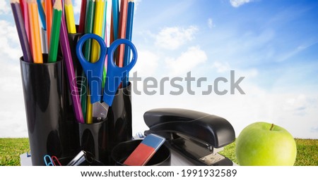 Digitally generated image of school equipment against green grass and blue sky in background. school and education concept