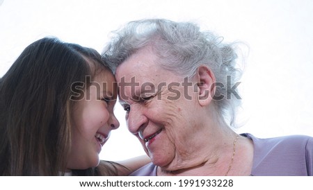 Cute little preschool girl smiling looks at old mature grandma nanny foreheads touching each other. Two generation grandparent and grandchild with enjoy, respect and warm relation in family. Close up Royalty-Free Stock Photo #1991933228