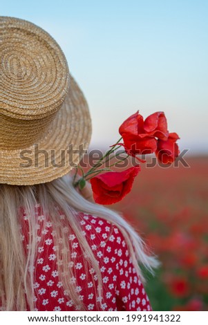 A girl in a straw hat from the back and red poppies flowers in her hand in a blooming poppy field. summer outdoor recreation and travel.