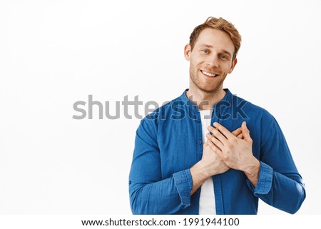 Right into my heart. Smiling attractive ginger guy holding hands on heart, being touched and happy, flattered by nice words, looking grateful and heartfelt, saying thank you, white background