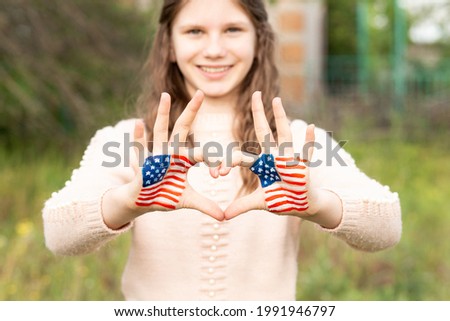 Hands of child painted in American flag color in heart shape, focus on hands. Patriotic holiday. Independence Day, Flag Day, 4th July, 14 June. Selective focus.Happy adorable little girl smiling and