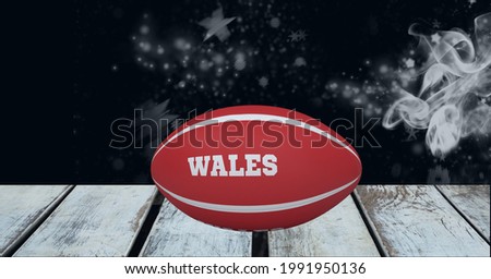 Red rugby ball with wales text over wooden surface against smoke effect on black background. sports tournament and competition concept