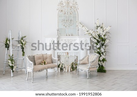 luxurious bright spacious guest room with beautiful chic furniture a huge floor-to-ceiling window in a royal style is decorated with green plants, white walls with stucco and a fireplace