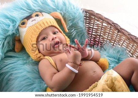 Indian five month baby lying in basket wearing diaper and monkey cap.