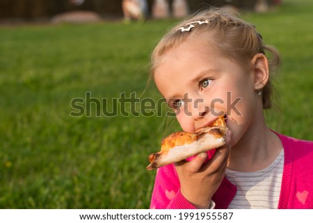 girl child eating pizza in the park on the street, close-up,green grass in the background and a place for text