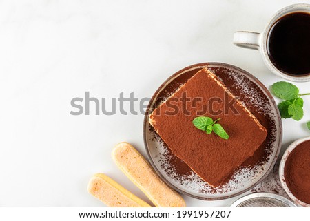 Italian homemade tiramisu cake with fresh mint on plate and coffee cup over white background. Top view with copy space. Delicious no bake dessert for tasty breakfast Royalty-Free Stock Photo #1991957207