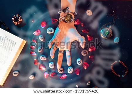 Astrology and horoscope. A woman's hand conjures stones with the signs of the zodiac, laid out in a circle and decorated with rose petals. The concept of divination and magic.