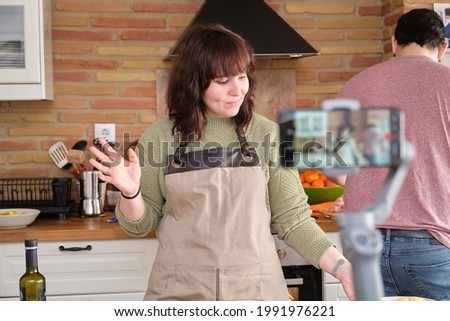 Young woman explaining a recipe and recording a video with her smartphone for her cooking channel. Content creator and influencer.