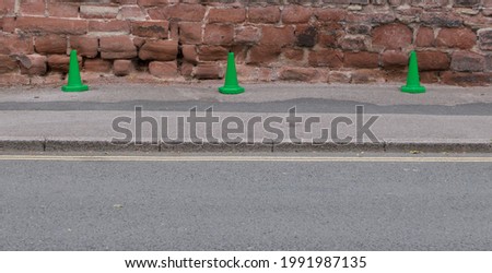 Three green plastic traffic cones beside road against historic wall