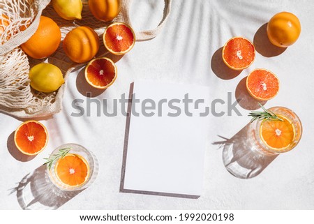 Summer vacation and holiday flat lay on white background. Cool citrus fruits cocktails, oranges, lemons and blank paper for your text. Palm shadow and sunlight, sun. Flat lay, top view, mockup Royalty-Free Stock Photo #1992020198