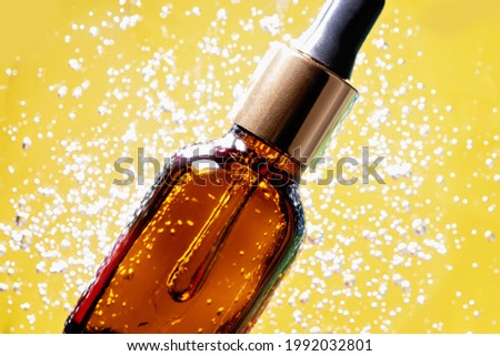 Close up amber glass bottle with essential oil or face serum placed on macro Aloe vera gel cosmetic texture illuminating yellow background with bubbles. Lemongrass gel skincare product.