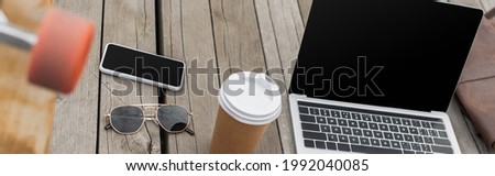gadgets with blank screen, sunglasses and paper cup on wooden table near blurred longboard, banner