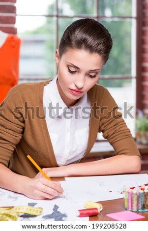 Working on creative fashion look. Beautiful young woman drawing fashion sketch while sitting at her working place 