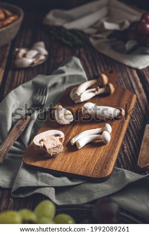 Dark photography of mushrooms, asparagus, bread, garlic and plums on a table of old wood. Vegetables recipe of for autumn or winter. Moody picture of seasonal cultivated fungus on a wooden table.