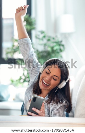 Shot of motivated young woman listening to music with smartphone while sitting on sofa at home.