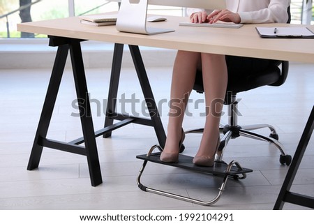 Woman using footrest while working on computer in office, closeup Royalty-Free Stock Photo #1992104291