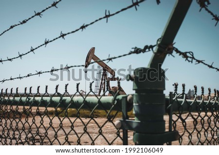 Oil field and pump jack behind barbed wire fence