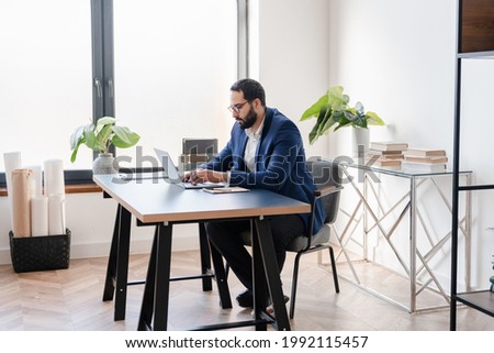 Successful mature Middle Eastern businessman working remotely, typing reports, signing contracts in home office on lockdown. Male freelancer doing paperwork multitasking at workplace