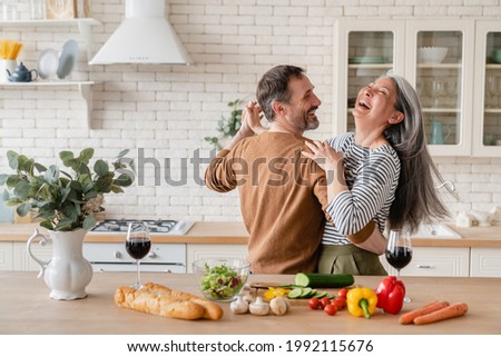 Happy cheerful middle-aged mature couple family parents dancing together in the kitchen, preparing cooking food meal for romantic dinner, spending time together. Active seniors Royalty-Free Stock Photo #1992115676