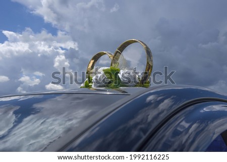 Two rings and white roses on the roof of a wedding car against a blue sky with clouds. Selective focus with copy space.