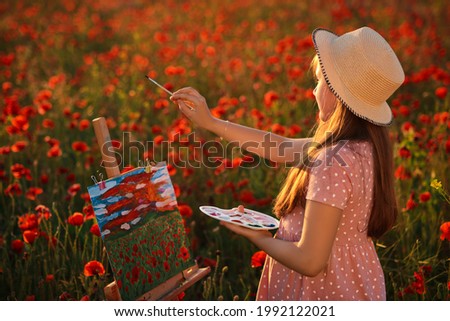 Little girl is standing in the field of red poppies On the Sunset and painting on the canvas placed on a drawing stand. Be a part of learning outside of the school in the nature park. Creative hobby