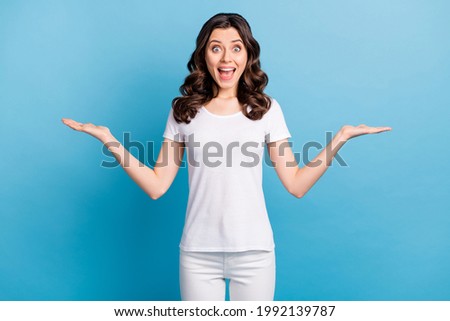 Photo of cute impressed young lady dressed white outfit holding arms empty space isolated blue color background