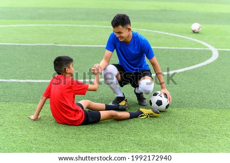 Asian teenager Football Players pulls the hand of a fallen player. Royalty-Free Stock Photo #1992172940