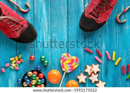 Saint Nicholas Day or Nikolaus Tag in German language. Traditional holiday in Germany, Europe. Decorative border - sweets, candy, cookies. Pair of shoes on blue turquoise textured wood.
