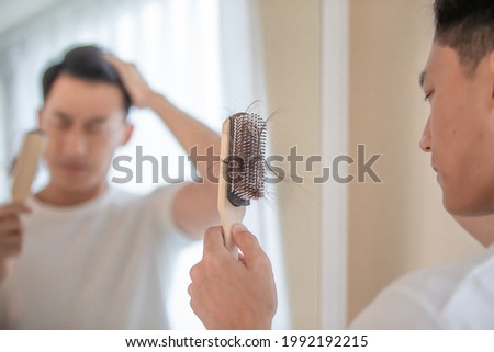 Asian man worry about his receding hairline and look in mirror with many hair on hairbrush Royalty-Free Stock Photo #1992192215