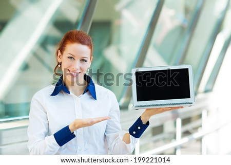 Closeup portrait smiling business woman holding laptop notebook computer, showing something on screen isolated background corporate office windows. Positive facial expression, emotion, attitude