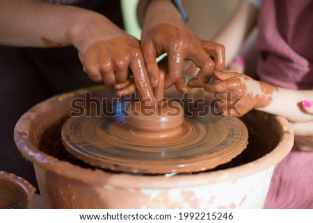 Master class for the child. Teacher hands show to kid how make ceramics dishes on potter wheel. Artist works with clay. Little girl sculpt cup clay